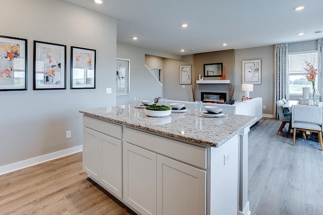 kitchen with light hardwood / wood-style flooring, white cabinetry, light stone counters, and a kitchen island