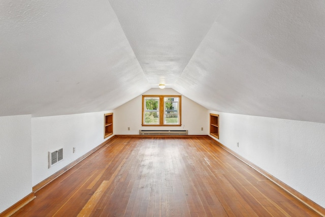 additional living space featuring built in features, baseboard heating, hardwood / wood-style flooring, and a textured ceiling