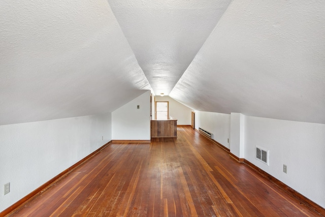 bonus room with lofted ceiling, dark wood-type flooring, baseboard heating, and a textured ceiling