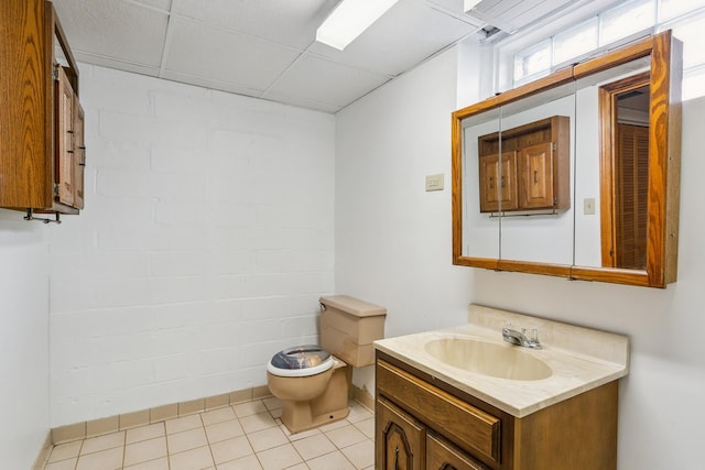 bathroom with brick wall, vanity, toilet, tile patterned floors, and a drop ceiling