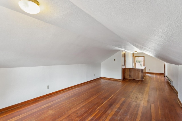 additional living space featuring a baseboard radiator, lofted ceiling, dark hardwood / wood-style floors, and a textured ceiling