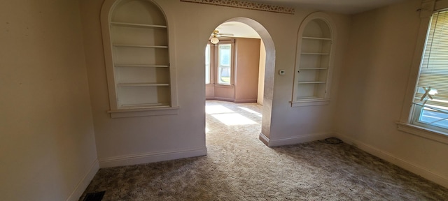 carpeted empty room with built in shelves and ceiling fan