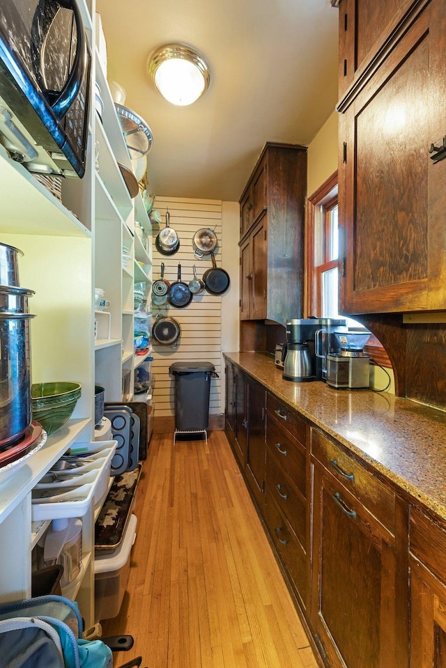 kitchen featuring dark brown cabinets, light hardwood / wood-style floors, and dark stone counters