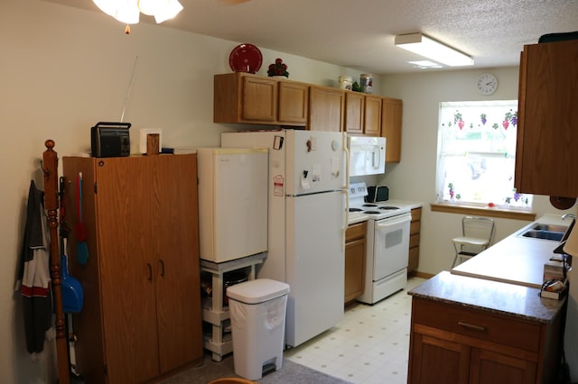 kitchen featuring brown cabinets, a sink, light floors, ceiling fan, and white appliances