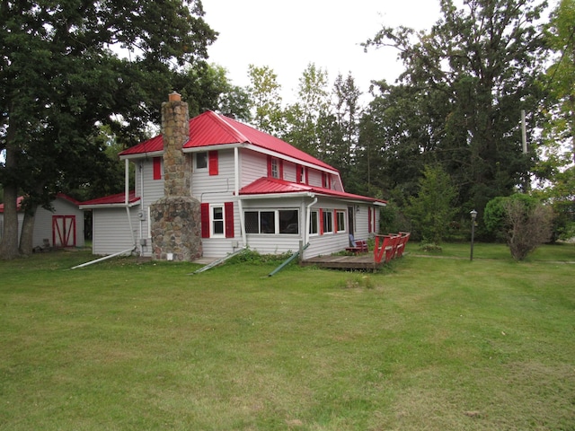 back of house with a yard, a chimney, and metal roof