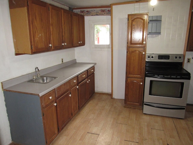 kitchen with brown cabinetry, light countertops, a sink, light wood finished floors, and stainless steel electric range oven