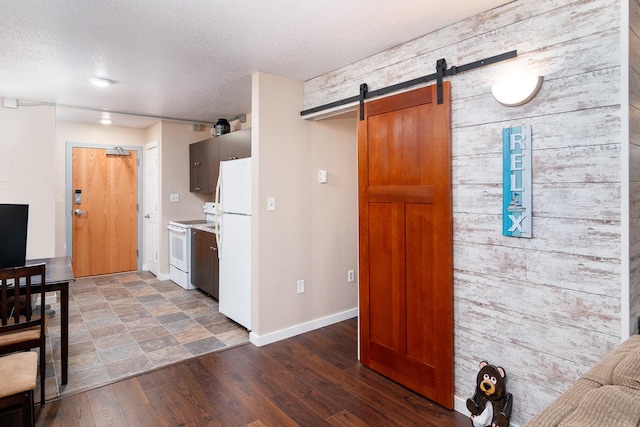 kitchen featuring a textured ceiling, dark wood-type flooring, a barn door, and white appliances