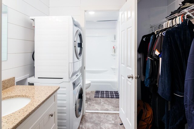 laundry area with wood walls, stacked washer and clothes dryer, and sink