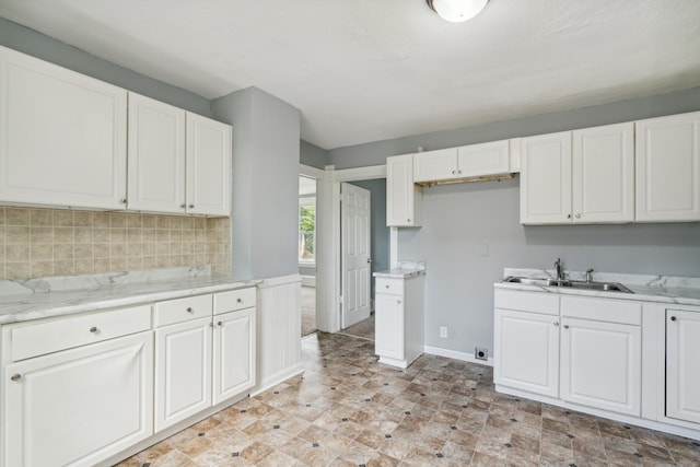 kitchen with white cabinets, light stone countertops, backsplash, and sink