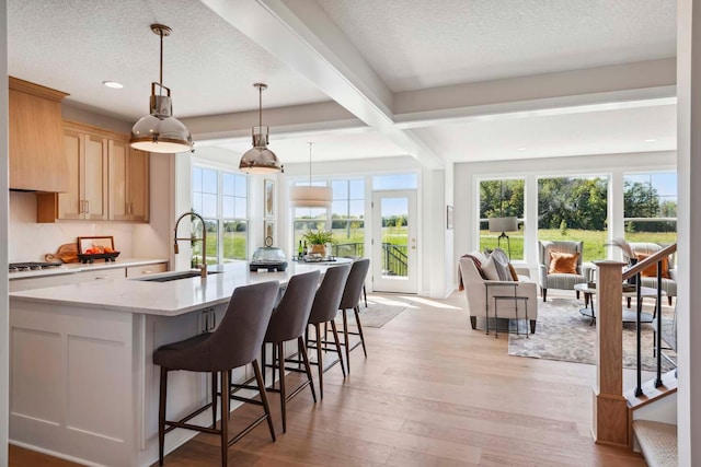 kitchen featuring light brown cabinetry, sink, light hardwood / wood-style floors, beamed ceiling, and decorative light fixtures