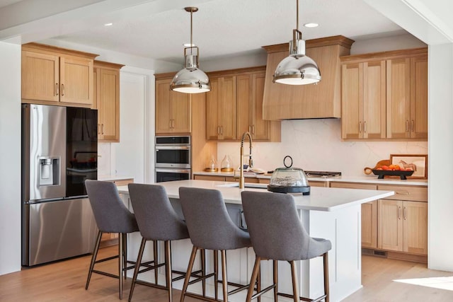 kitchen with light hardwood / wood-style floors, decorative light fixtures, a kitchen island with sink, and stainless steel appliances