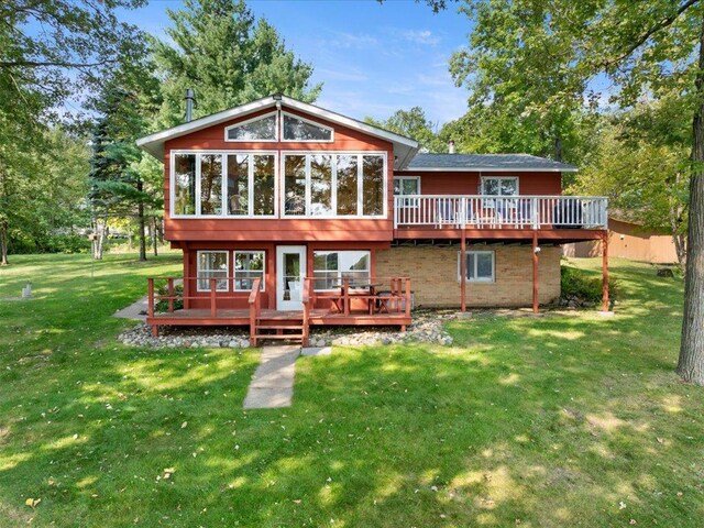 rear view of property with a sunroom, a lawn, and a wooden deck