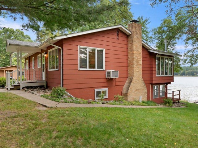 view of property exterior with a lawn, a water view, and a wall unit AC