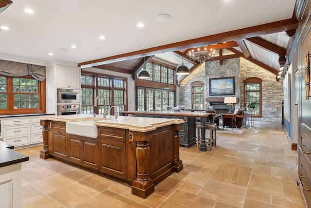 kitchen featuring sink, white cabinets, a center island with sink, and lofted ceiling with beams