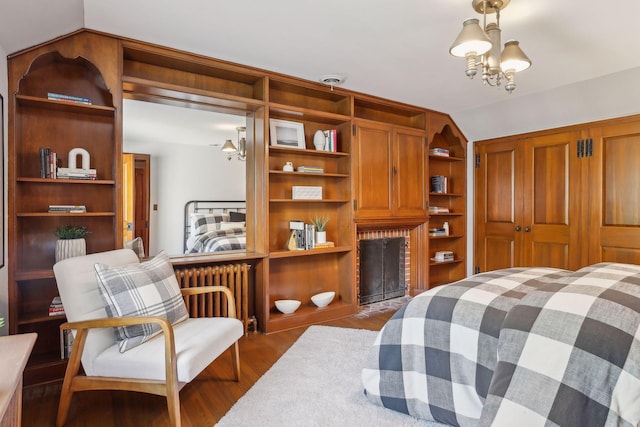 bedroom with lofted ceiling, a brick fireplace, wood-type flooring, an inviting chandelier, and radiator heating unit