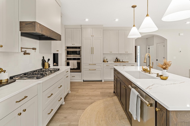 kitchen featuring appliances with stainless steel finishes, custom exhaust hood, a center island with sink, and light stone countertops