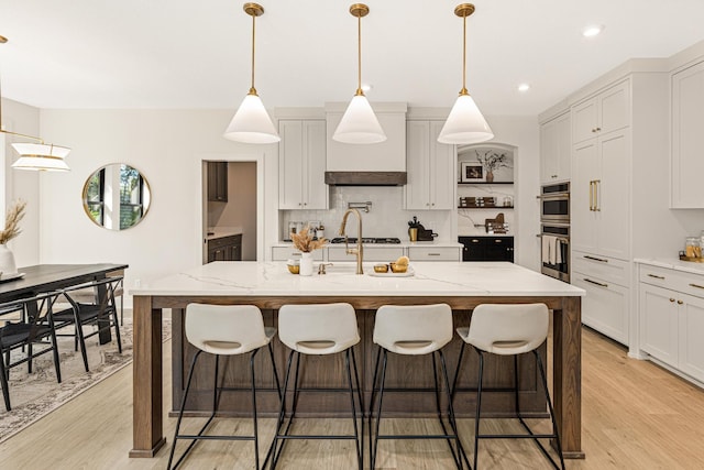 kitchen featuring a kitchen breakfast bar, light stone countertops, a kitchen island with sink, and light hardwood / wood-style flooring