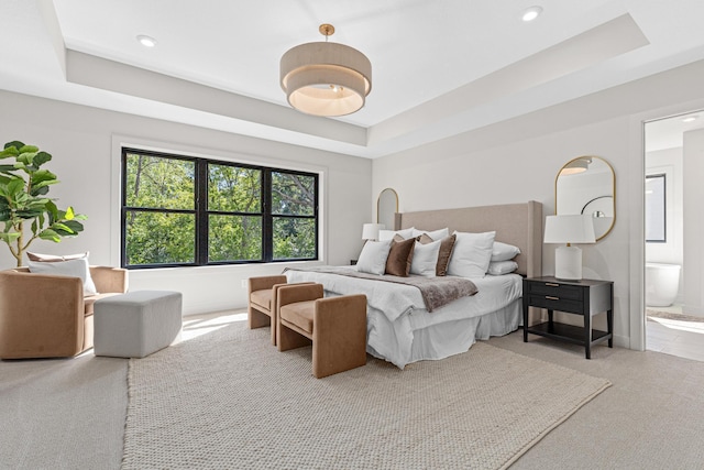 bedroom featuring light carpet, a raised ceiling, and connected bathroom