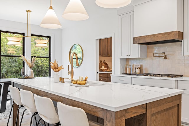 kitchen featuring a center island, decorative light fixtures, light stone counters, custom exhaust hood, and white cabinetry