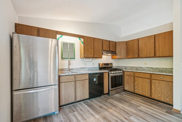 kitchen with sink, a textured ceiling, vaulted ceiling, appliances with stainless steel finishes, and light wood-type flooring