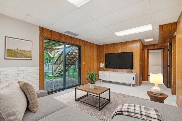 living room featuring a drop ceiling, light colored carpet, and wooden walls