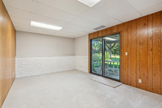 carpeted empty room featuring a drop ceiling and wooden walls