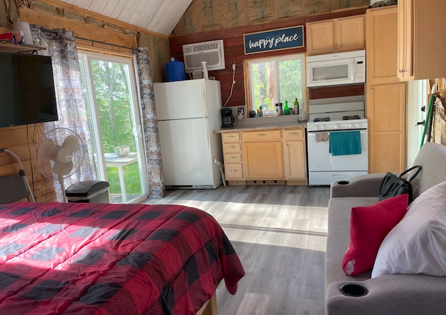 bedroom with a wall mounted AC, vaulted ceiling, white refrigerator, and multiple windows