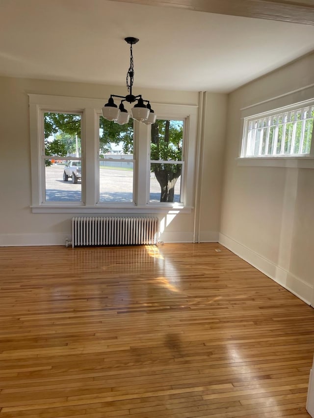unfurnished dining area with hardwood / wood-style floors, baseboards, an inviting chandelier, and radiator