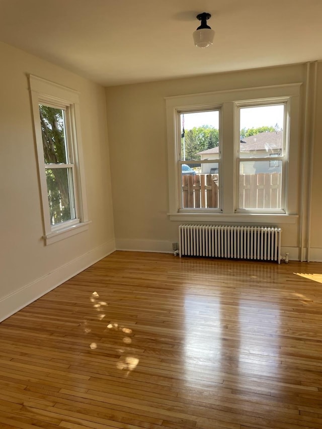 empty room with baseboards, wood finished floors, and radiator heating unit