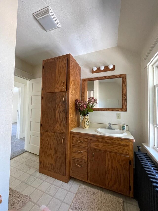 bathroom with vanity, radiator, lofted ceiling, tile patterned floors, and visible vents
