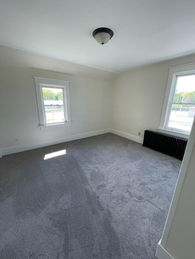 carpeted spare room with baseboards, vaulted ceiling, radiator heating unit, and a healthy amount of sunlight