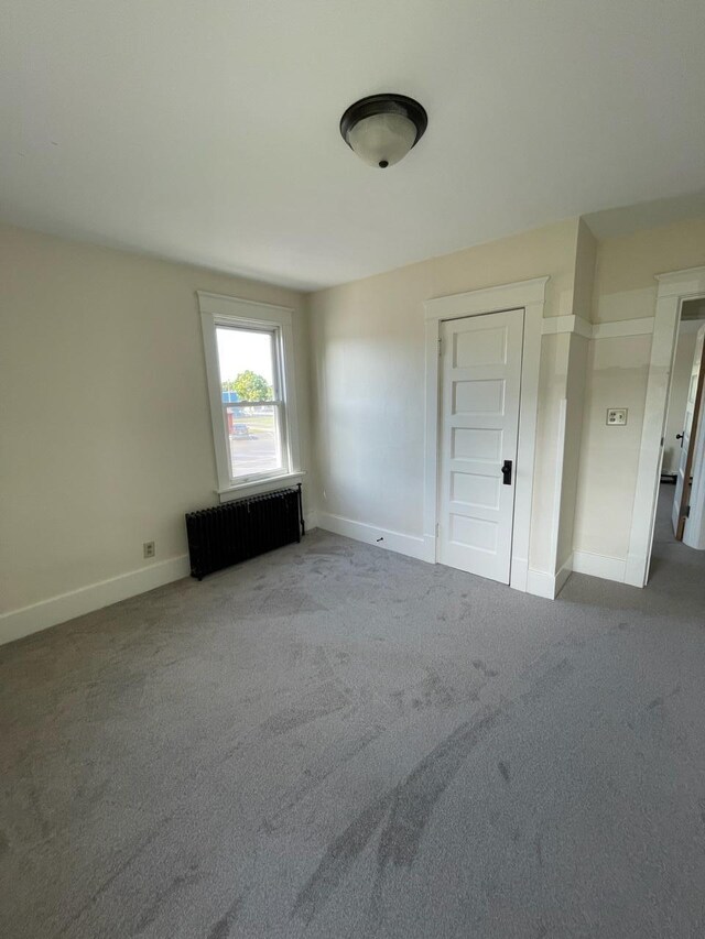 carpeted spare room featuring radiator and baseboards