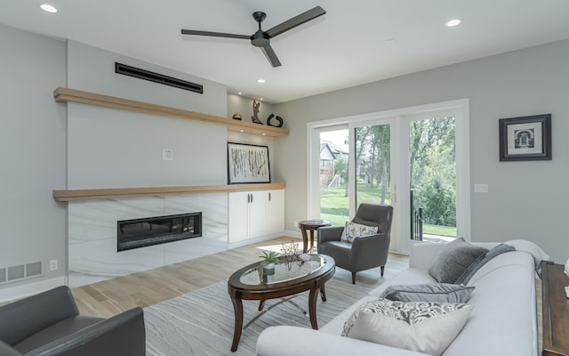 living room featuring ceiling fan, a fireplace, and light hardwood / wood-style floors