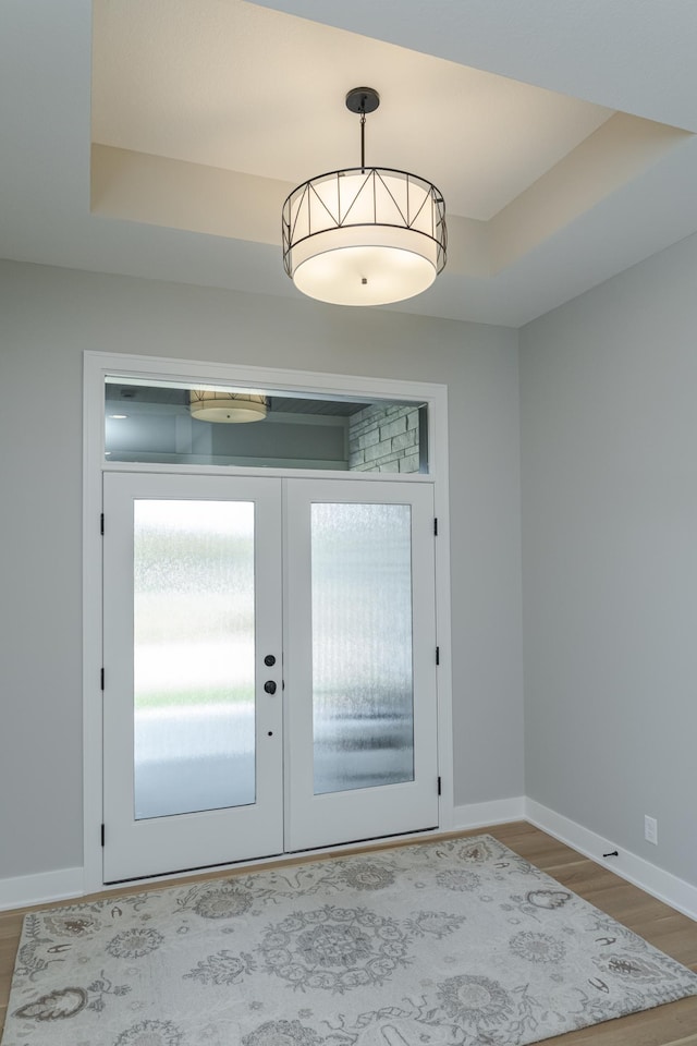 entryway with a tray ceiling, french doors, and light wood-type flooring