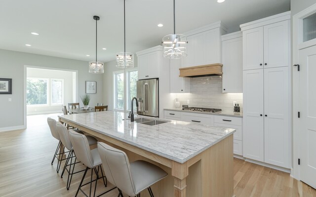 kitchen with light stone countertops, an island with sink, stainless steel appliances, sink, and white cabinetry