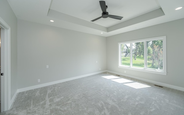 spare room with a tray ceiling, light carpet, and ceiling fan