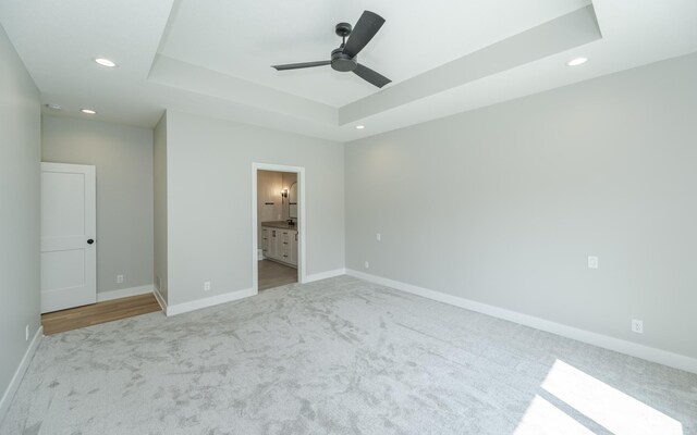 unfurnished bedroom featuring light colored carpet, connected bathroom, ceiling fan, and a tray ceiling