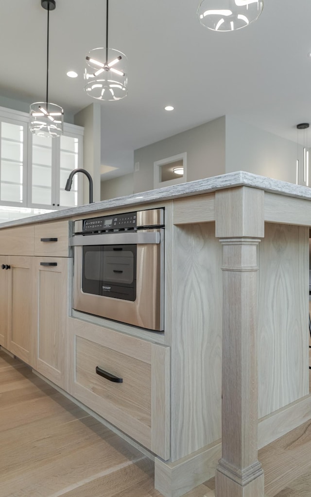 kitchen with pendant lighting, oven, an inviting chandelier, light brown cabinets, and light hardwood / wood-style floors