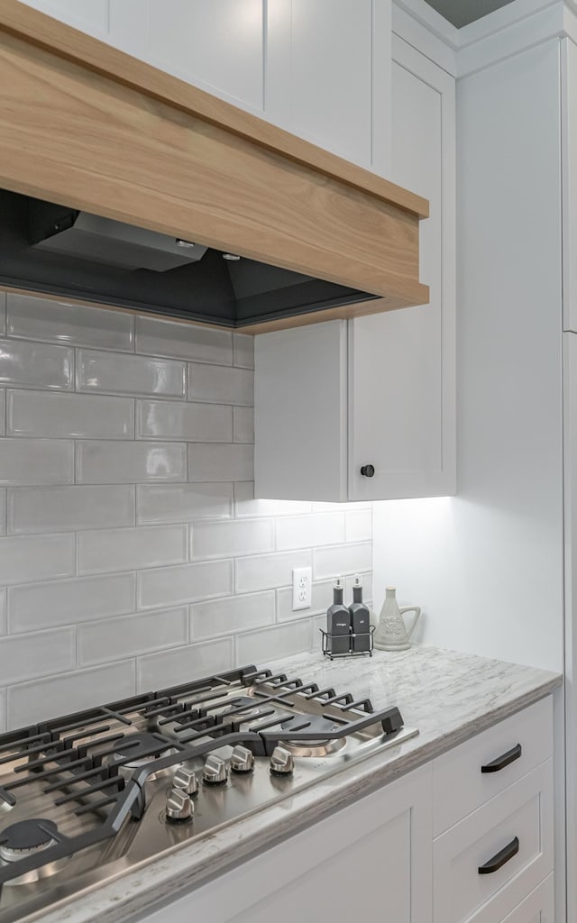 kitchen with stainless steel gas stovetop, light stone counters, custom exhaust hood, white cabinetry, and decorative backsplash