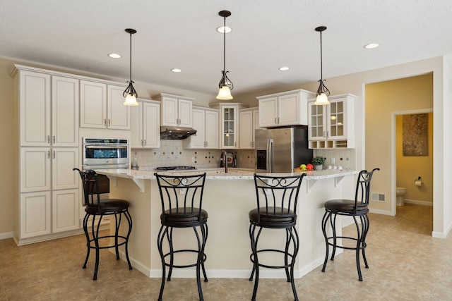 kitchen with a kitchen island with sink, hanging light fixtures, light stone countertops, tasteful backsplash, and stainless steel appliances