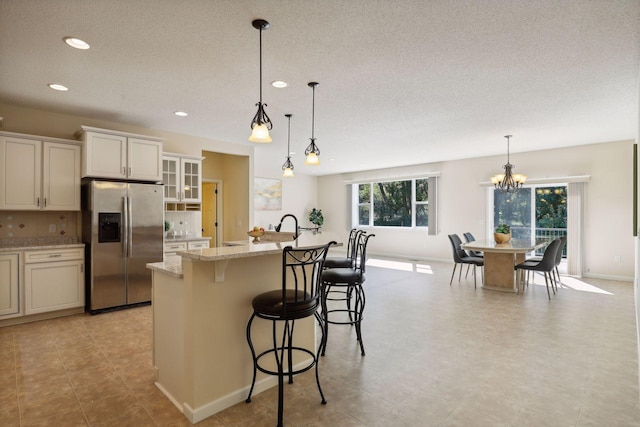 kitchen with stainless steel fridge, a kitchen island with sink, decorative light fixtures, a chandelier, and a breakfast bar area