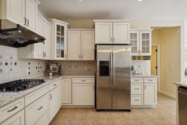 kitchen featuring a textured ceiling, decorative backsplash, light stone counters, and stainless steel appliances