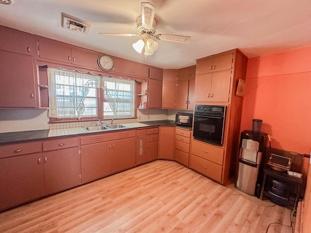 kitchen featuring black oven, sink, ceiling fan, and light hardwood / wood-style flooring