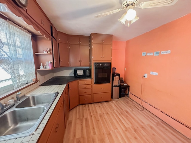 kitchen with ceiling fan, sink, a baseboard heating unit, black appliances, and light wood-type flooring