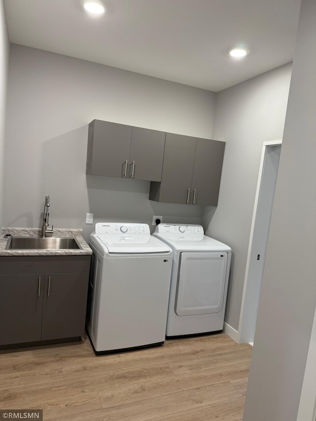 clothes washing area featuring sink, cabinets, washing machine and clothes dryer, and light wood-type flooring