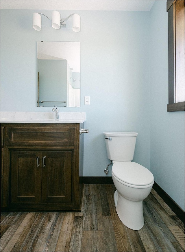 half bathroom featuring vanity, toilet, wood finished floors, and baseboards