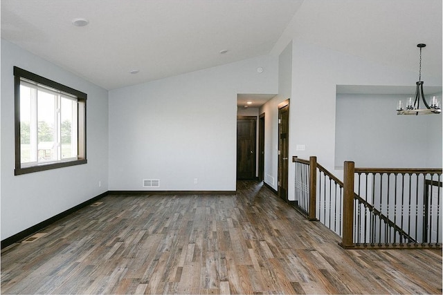 spare room featuring wood finished floors, visible vents, baseboards, an inviting chandelier, and lofted ceiling