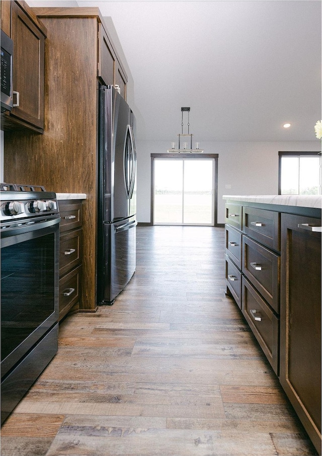 kitchen with dark brown cabinetry, hanging light fixtures, light wood-type flooring, and appliances with stainless steel finishes