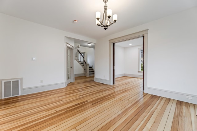 unfurnished room featuring a notable chandelier, visible vents, baseboards, light wood-style floors, and stairs