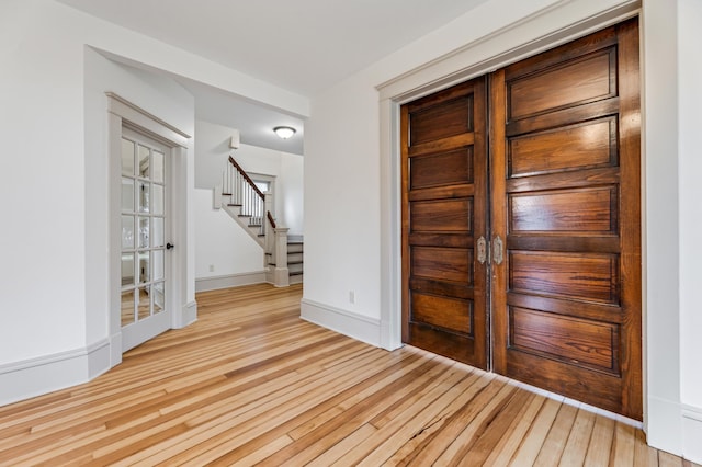 entrance foyer with stairs, baseboards, french doors, and light wood-style floors